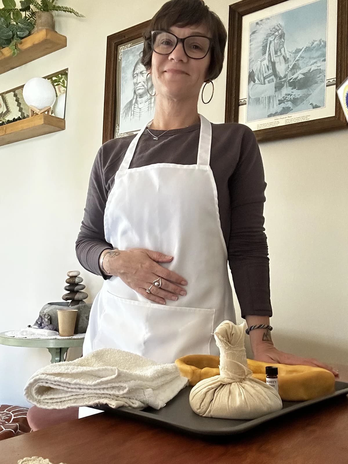 Nicole standing behind a tray set for an Ayurvedic body treatment, with an herbal poultice, towel, and oil